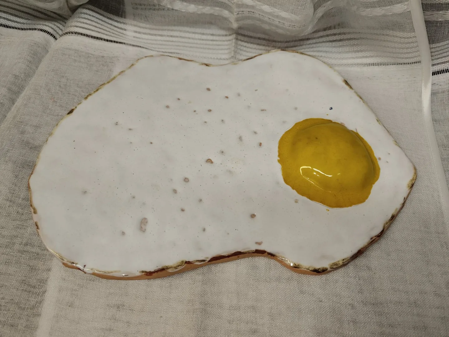 Ceramiczna forma przypominająca jajko sadzone, z jasną powierzchnią i żółtym środkiem.